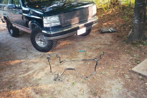 1994 Ford Bronco - A dark green Ford F-Series truck is parked outdoors with its front end visible and steering components laid out on the ground.
