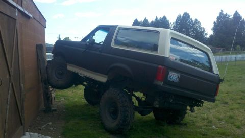 1988 Ford Bronco - This lifted 1988 Ford Bronco is shown leaning against a wooden structure, highlighting its off-road capabilities.
