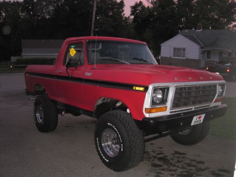 1979 Ford Bronco - Red lifted Ford F-100 short-bed 4x4 pickup with chrome grille, black side stripe and BFGoodrich tires, parked in a suburban driveway at dus…