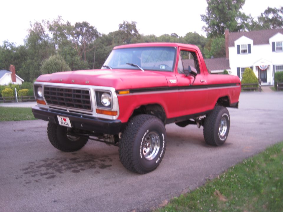 1979 Ford Bronco lifted with large tires, parked on asphalt in front of a house