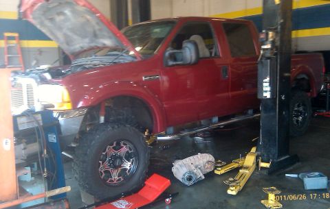 2000 Mercury Grand Marquis - A red pickup truck is in a repair shop with its hood open and transmission removed.
