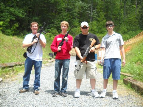 2012 Ford Mustang - Four men pose with firearms at an outdoor shooting range, with trees and a safety fence in the background.