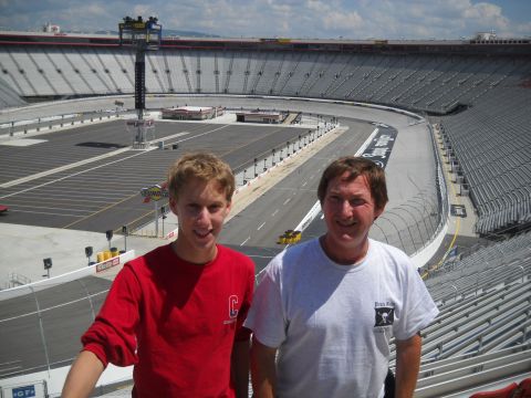2012 Ford Mustang - Two men pose for a photo at a large stadium with a race track in the background.