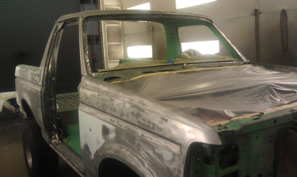 Truck body stripped down, covered in primer and plastic sheeting, in a workshop