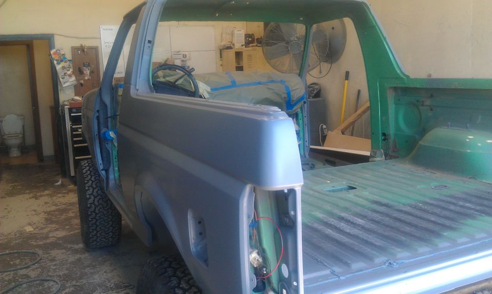 Gray and green Ford Bronco body in a garage, undergoing repairs. The rear bed is green, and the cab is gray primer