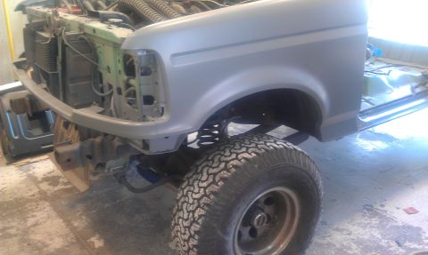 1995 Ford Bronco - Front end of a 1992 Ford Bronco undergoing repairs, showing exposed engine components and primer on the fender.