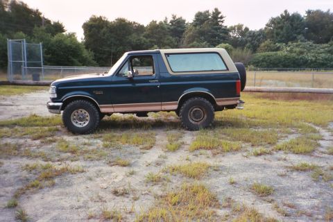 1994 Ford Bronco - This 1994 Ford Bronco is seen from the side, parked outdoors in a grassy area with trees in the background.