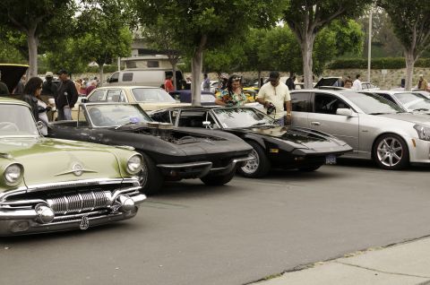 2006 Cadillac STS - A collection of vehicles, ranging from vintage to modern, are parked together on a paved surface under trees.