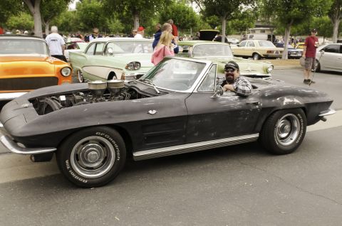 2006 Cadillac STS - A man poses in a black 1963 Corvette convertible with its hood open, revealing the engine, at an outdoor car show.