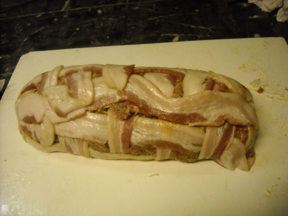 Meatloaf wrapped in bacon on a white cutting board