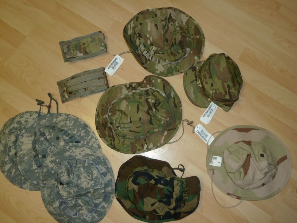 Various camouflage bucket hats and pouches on a wooden floor. One hat is desert camouflage, others are woodland or multicam