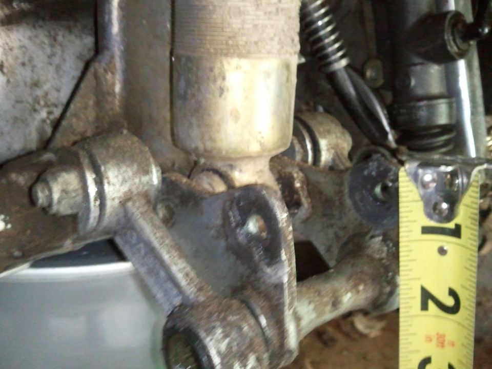 Close-up of a rusty suspension component with a yellow tape measure indicating 1-2 inches