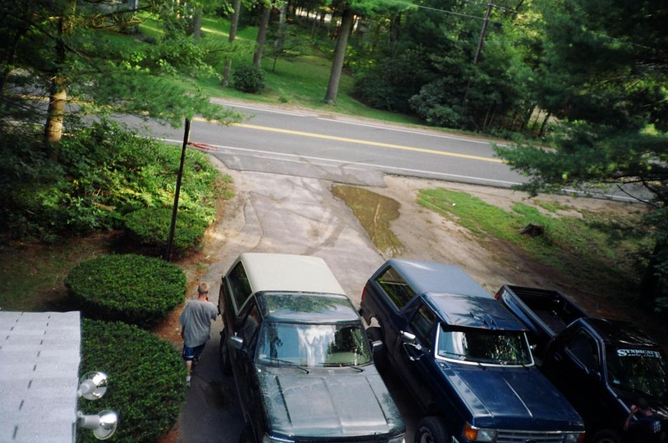 Overhead view of a green Ford Bronco with tan top parked beside two pickups on a dirt driveway