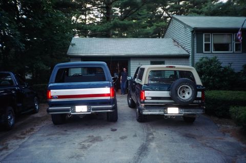 1994 Ford Bronco - Two Ford Broncos are parked in a driveway in front of a house and garage.