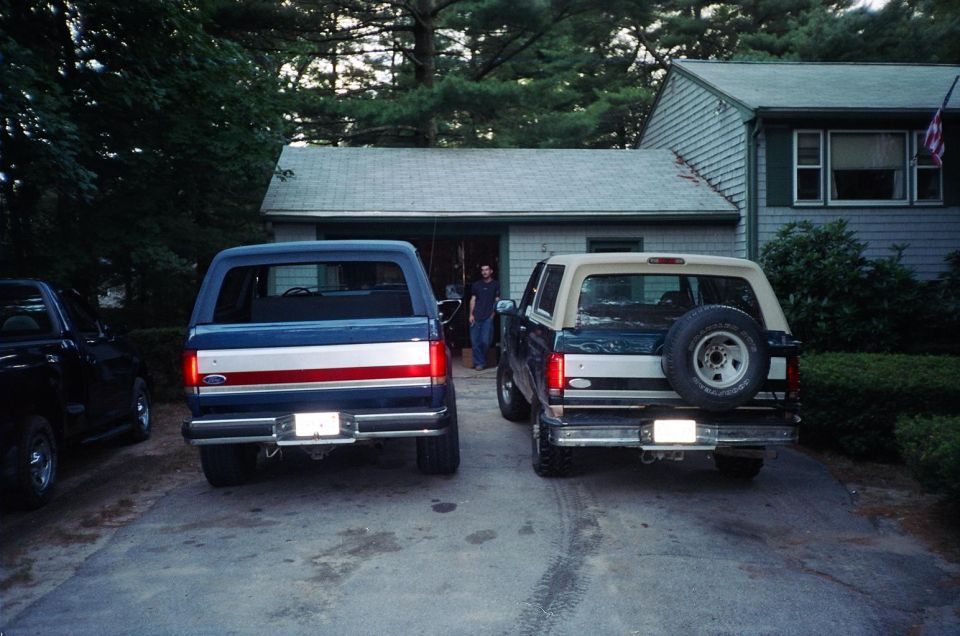 Rear view of a blue Ford Bronco and a green Bronco with tan top parked in a driveway