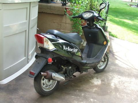 2008 Yamaha Zuma - A black scooter is parked on a concrete surface next to a large storage unit, with greenery in the background.