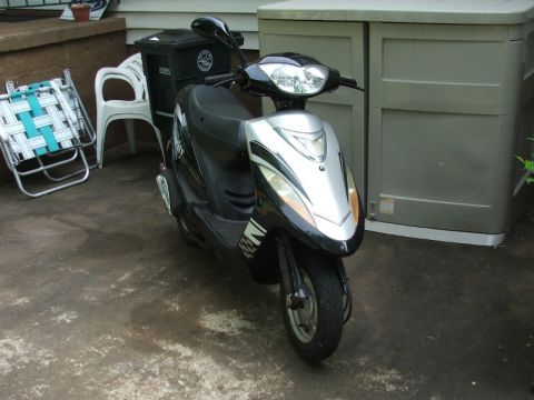 2008 Yamaha Zuma - A black and silver scooter is parked on a concrete patio next to outdoor furniture and a storage shed.