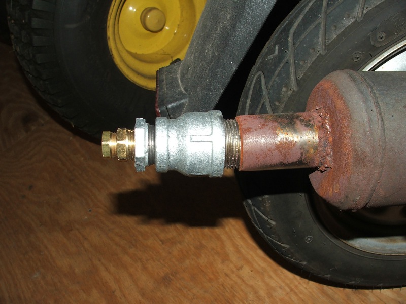 Close-up of a custom exhaust pipe with a brass fitting attached to a rusty metal pipe, next to a scooter tire and yellow wheel