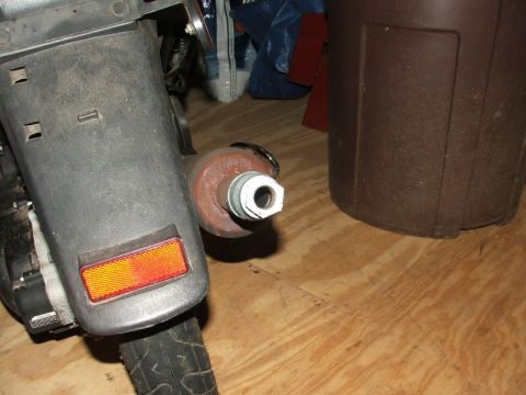 2008 Yamaha Zuma - A scooter's rear fender and exhaust pipe are visible against a wooden floor and a brown bin.