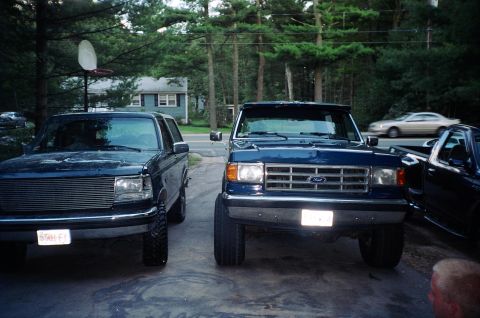 1994 Ford Bronco - Two SUVs and a pickup truck are parked in a driveway, with a house and trees in the background.