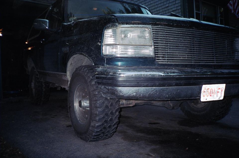Front of dark muddy Ford Bronco or F-series with mud tires at night