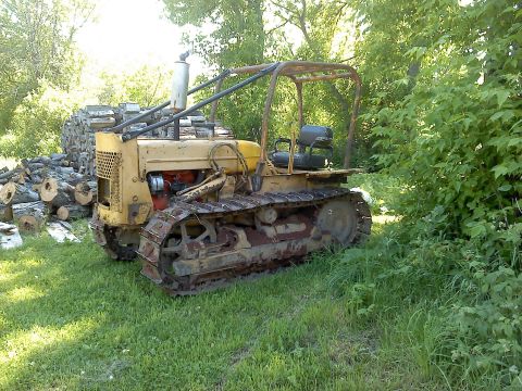 1963 Hummer H3 - This vintage crawler tractor is parked outdoors next to a stack of firewood, with trees and foliage in the background.