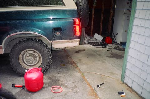 1994 Ford Bronco - A red gas can is connected to the fuel tank of a green Ford Bronco, likely for refueling or transferring fuel.