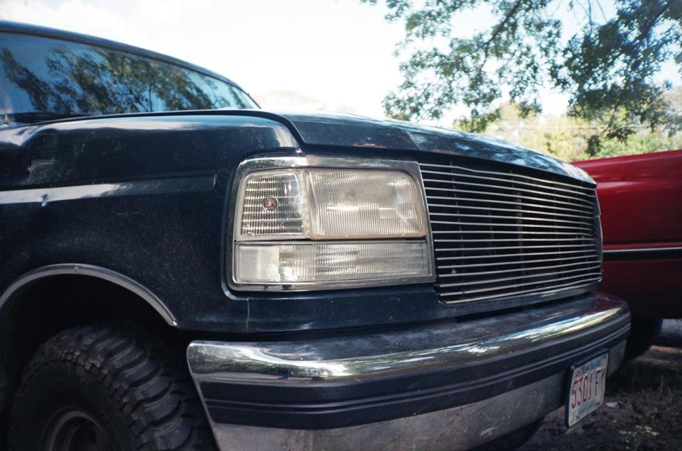 Front corner close-up of a dark green Ford with billet grille, clear headlight and chrome bumper