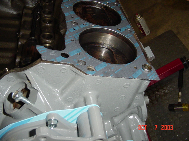 Engine block bare deck with two cylinder bores exposed, painted gray, gasket and spray can nearby