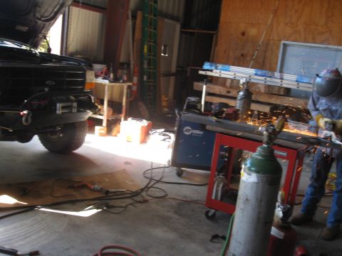 1994 Ford Bronco - A black Ford Bronco is partially visible in a workshop setting, with a person welding in the background.