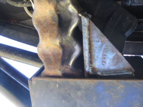 1994 Ford Bronco - This image shows a close-up of a rusted metal suspension component with visible welds and a blue metal frame below.