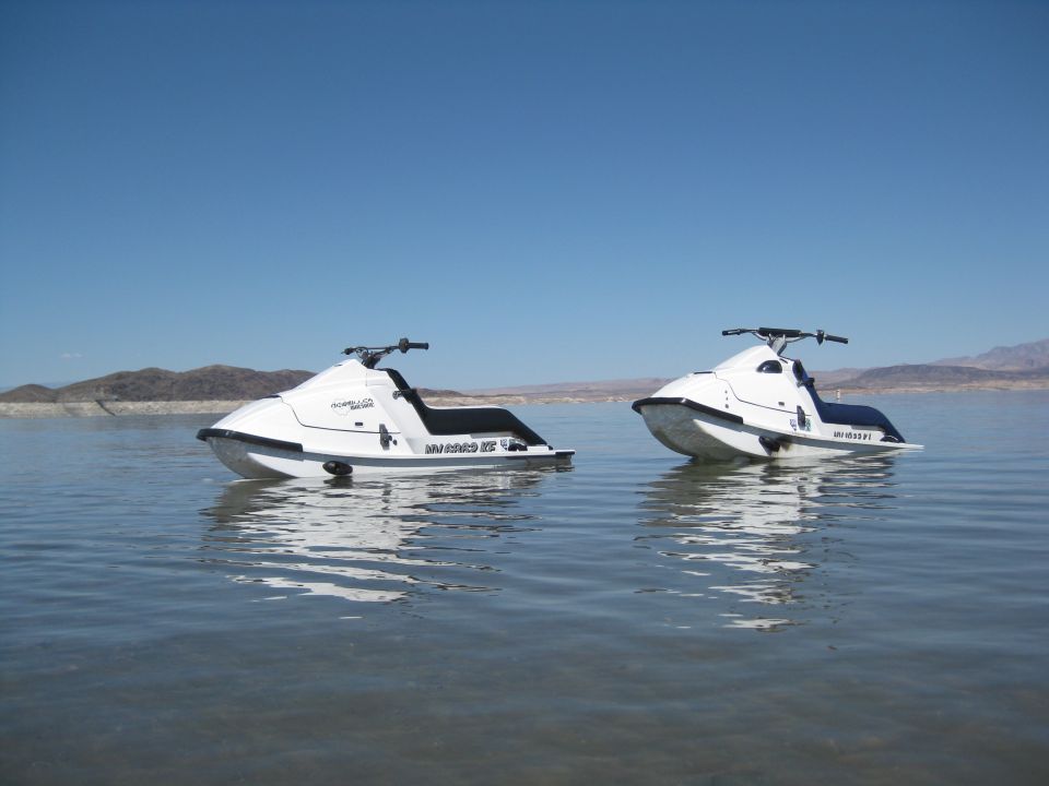 Two white stand-up jet skis floating on calm water with desert mountains behind
