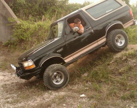 1994 Ford Bronco - 1994 Ford Bronco navigates a challenging off-road trail, climbing a steep dirt embankment.