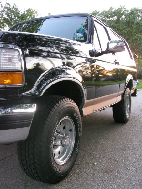 1994 Ford Bronco - A black 1994 Ford Bronco is viewed from a low angle, highlighting its front quarter and side profile.