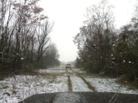 1994 Ford Bronco - An orange SUV travels down a snow-covered dirt road, surrounded by trees.