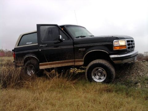 1994 Ford Bronco - A black Ford Bronco with a tan top is parked on a dirt mound with grass surrounding it.