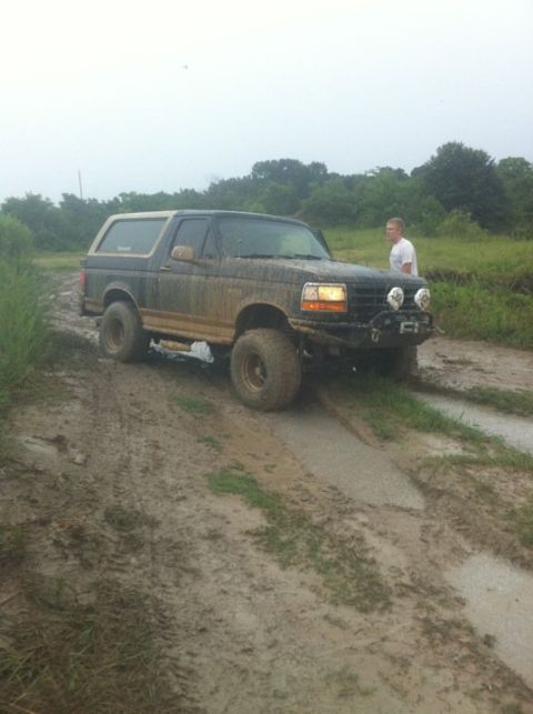 1994 Ford Bronco - A person watches a muddy 1994 Ford Bronco navigate a wet, dirt path.