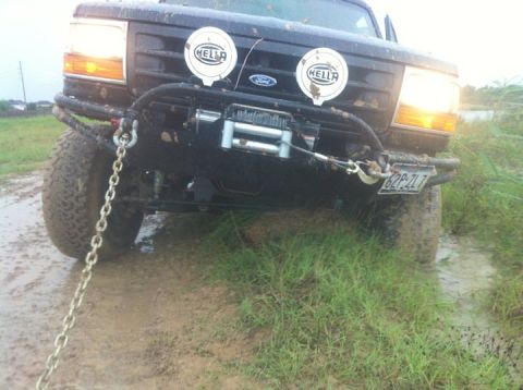 1994 Ford Bronco - A black Ford Bronco is stuck in muddy terrain, equipped with a winch and Hella lights.