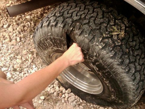 1994 Ford Bronco - A hand presses on a flat tire, revealing the damage.