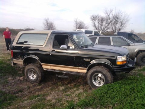1994 Ford Bronco - Black 1994 Ford Bronco with tan trim, parked on uneven terrain with other vehicles behind it.