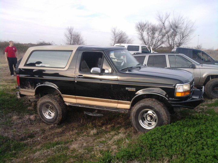 1994 Ford Bronco parked off-road with a person standing nearby; other vehicles visible in background