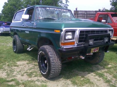 1979 Ford Bronco - A green 1978 Ford Bronco with a white top is parked on grass next to other vehicles.