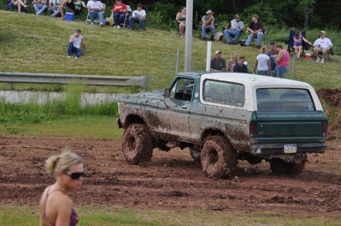 1979 Ford Bronco - A muddy 1979 Ford Bronco navigates a dirt track with spectators watching from a grassy embankment.
