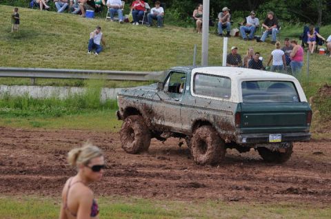 1979 Ford Bronco - Muddy Ford Bronco navigates a mud pit event with onlookers in the background.