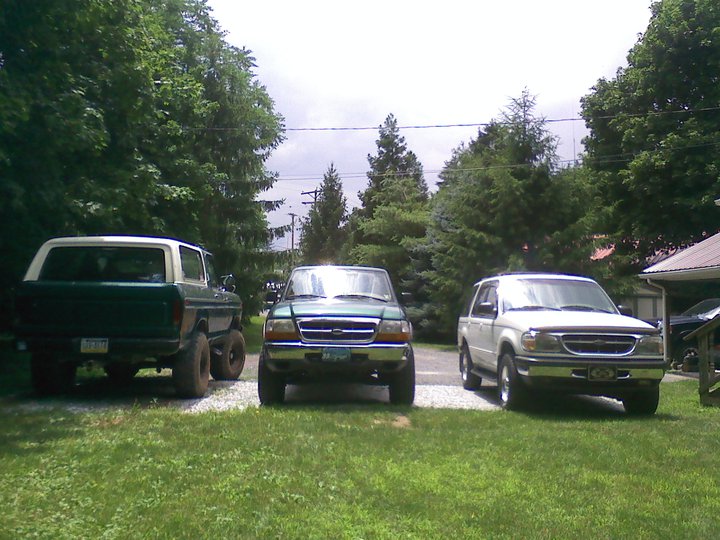 Green 1979 Ford Bronco with white top, lifted suspension, and large tires, parked next to two other SUVs
