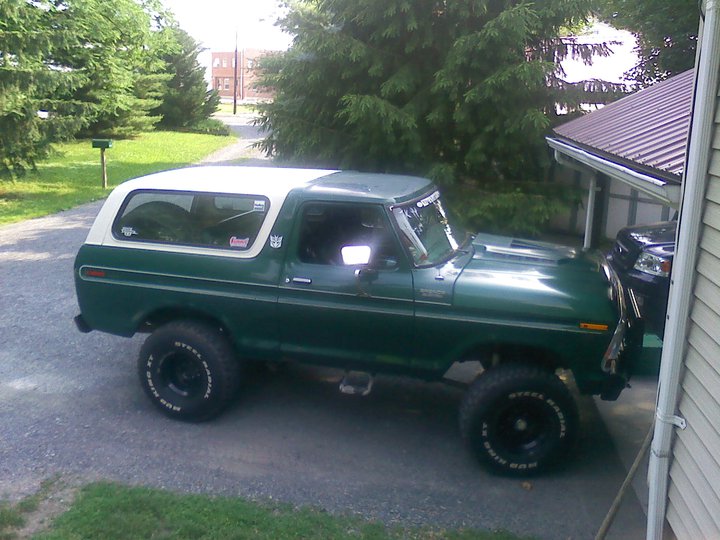 Green 1978 Ford Bronco with white removable top parked on gravel driveway