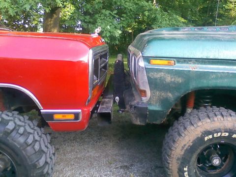 1979 Ford Bronco - Two lifted trucks are parked very close, their front bumpers nearly touching.