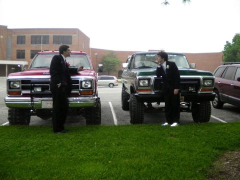 1979 Ford Bronco - Two lifted pickup trucks, a red Dodge and a green Ford, are parked on grass with two young men in suits.