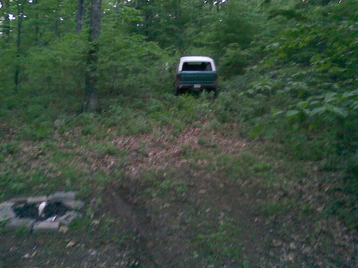 Green and white SUV parked on a grassy hill in a wooded area