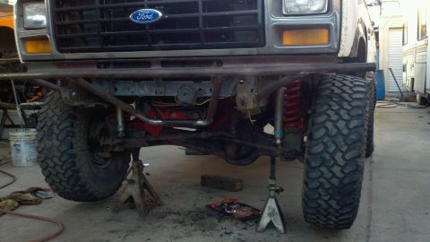 1982 Ford Bronco - The front of a Ford truck is elevated on jack stands, revealing its suspension system and off-road tires.